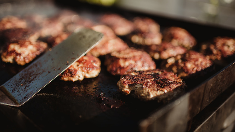 Burger patties on flat-top grill with metal spatula.