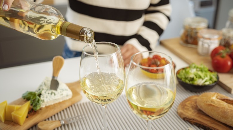 Hand pouring a glass of white wine on a kitchen counter