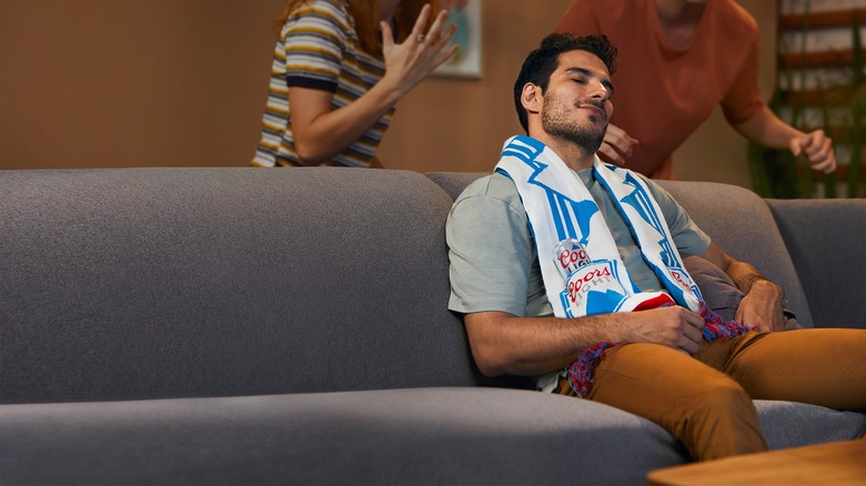 Man sits on couch wearing Coors Light Scarf