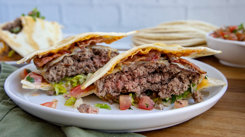 A burger between two small tortillas on a white plate 