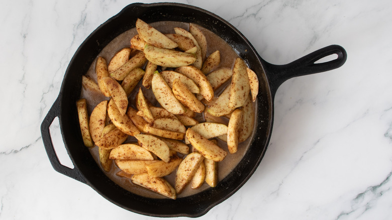 sliced apples and brown liquid in a black frying pan