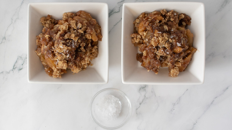 cooked apples with crumbly brown topping in two square white bowls next to a small clear bowl of salt