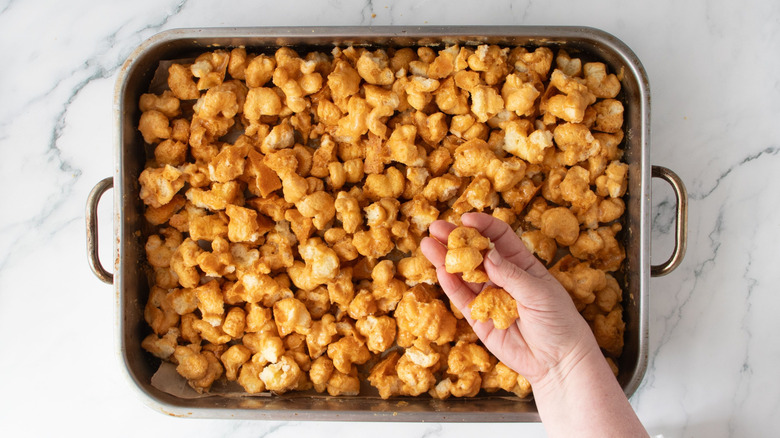 Hand holding caramel coated puffcorn over roasting pan
