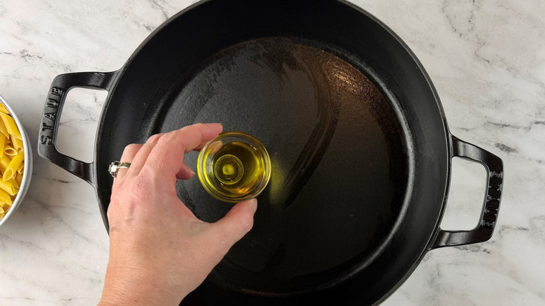 hand holding oil over a black frying pan
