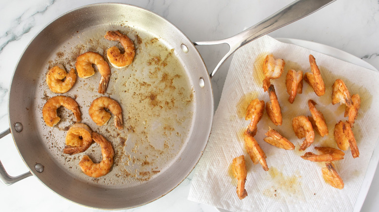 Shrimp in skillet next to shrimp on paper towel