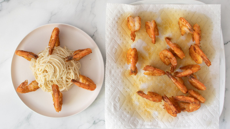Shrimp scampi on plate next to shrimp on paper towel