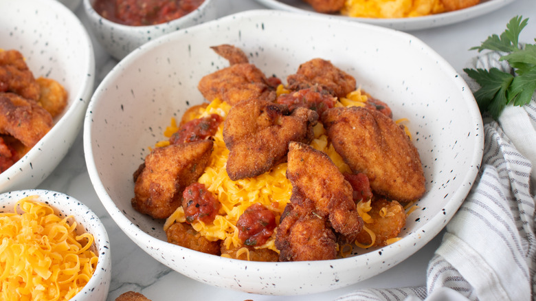 chicken nuggets, fried potatoes, scrambled eggs and cheese in a speckled white bowl