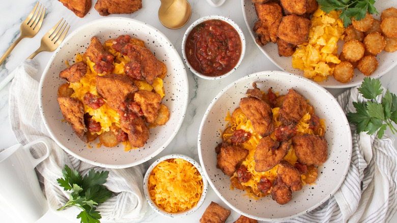 chicken nuggets, fried potatoes, scrambled eggs and cheese in two speckled white bowls