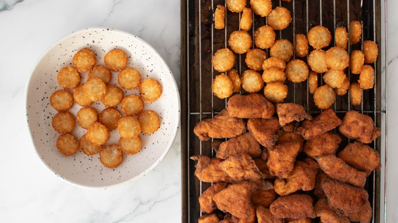 fried potato nuggets in a speckled white bowl next to potatoes and chicken nuggets on wire rack