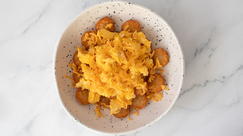 fried potatoes, scrambled eggs and cheese in a speckled white bowl