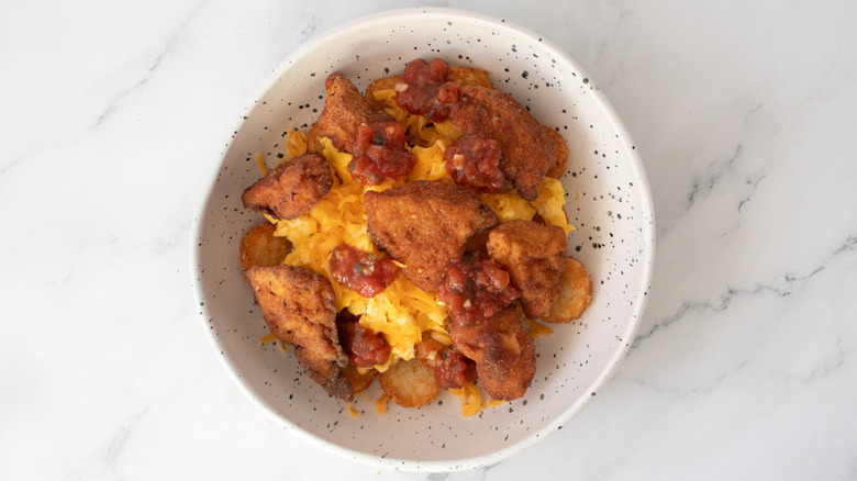 chicken nuggets, fried potatoes, scrambled eggs and cheese in a speckled white bowl