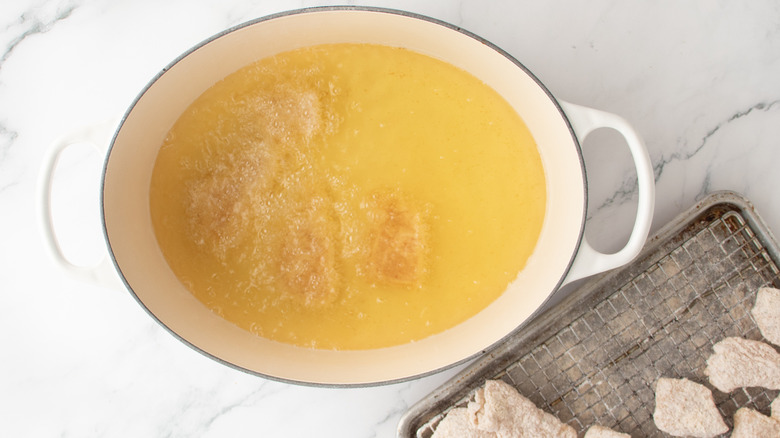 floured chicken pieces submerged in oil in a white pot