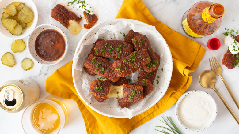 Nashville hot mozzarella sticks in bowl surrounded by various sauces and sides