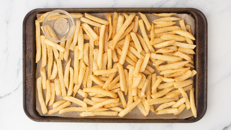 Fries and small bowl of seasoning on baking sheet