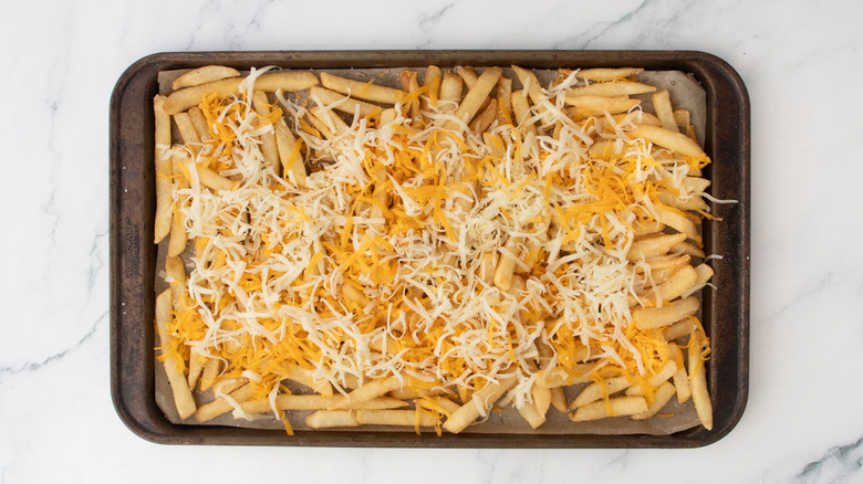 Fries on baking sheet topped with shredded cheese