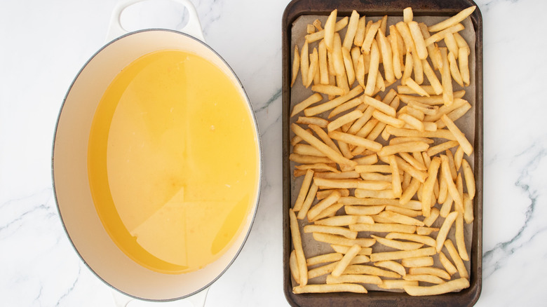 Large pot of oil next to fries on baking sheet