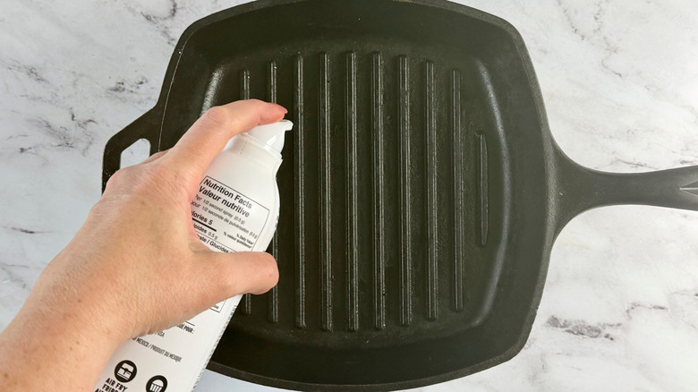 Hand spraying grill pan with cooking spray