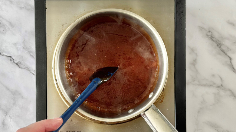Hand using rubber spatula to stir sauce in saucepan
