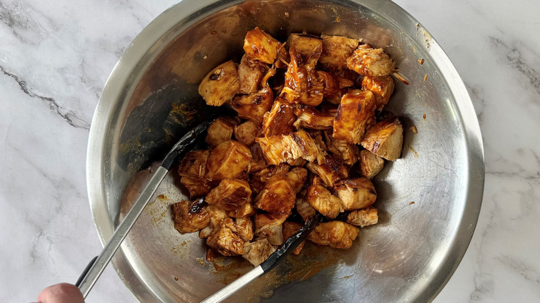 Tongs tossing chicken bites in sauce