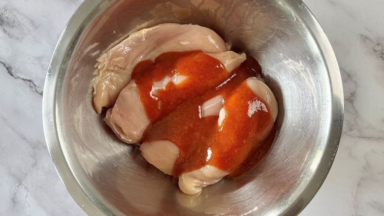 Raw chicken breasts and red sauce in bowl