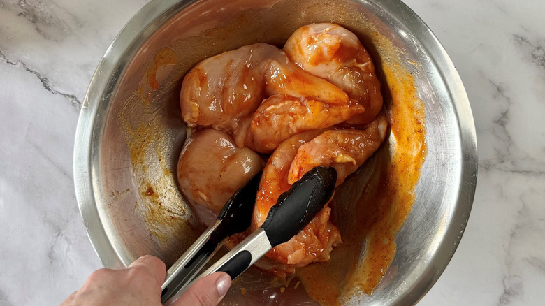 Tongs tossing chicken breasts in sauce