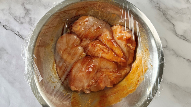 Saucy chicken in bowl covered with plastic wrap