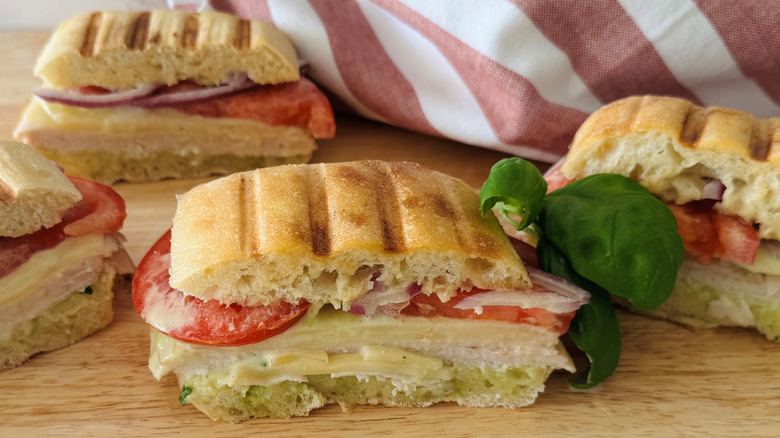 turkey, tomato, and cheese sandwiches on a wooden board with a striped towel
