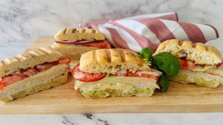 turkey, tomato, and cheese sandwiches on a wooden board with a striped towel