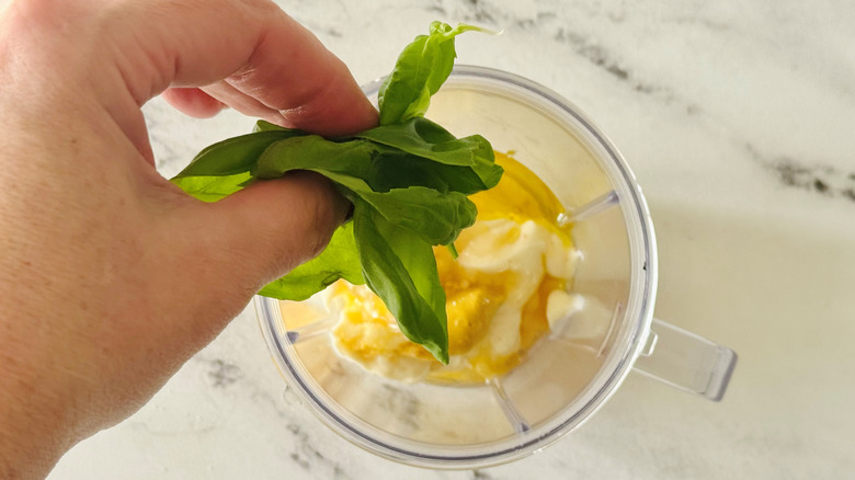 hand holding basil leaves above mayonnaise and mustard