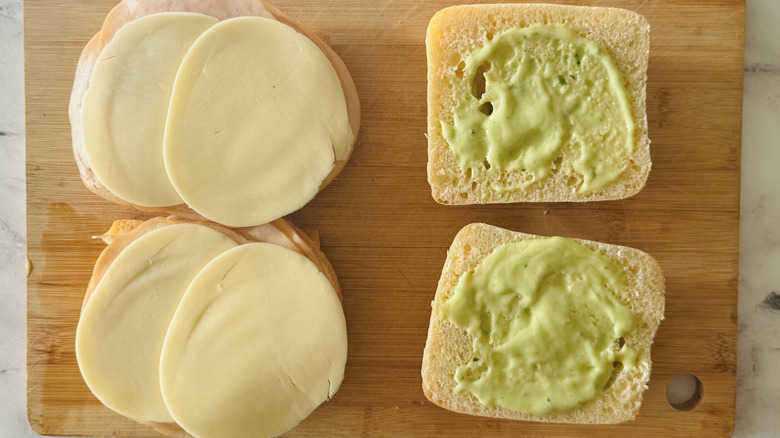 bread topped with green spread, meat, and cheese
