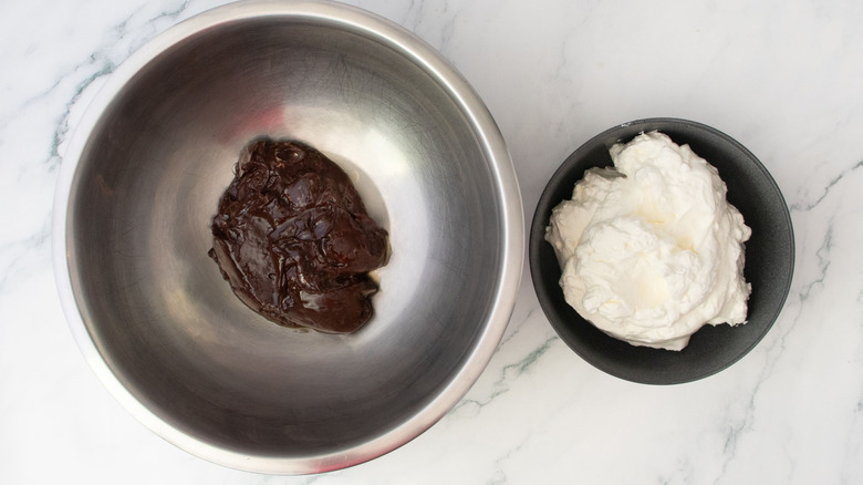 Thick chocolate mixture in bowl next to whipped cream in bowl