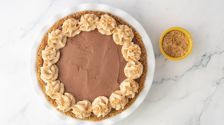 Chocolate peanut butter mousse pie with graham cracker crumbs next to small bowl of crumbs