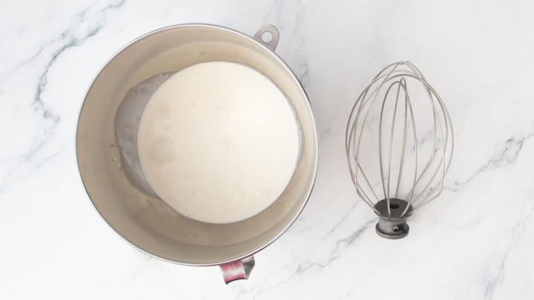 Heavy cream in stand mixer bowl next to whisk attachment