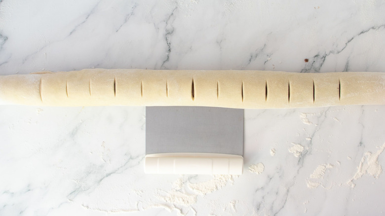 Dough log with shallow slices next to bench scraper