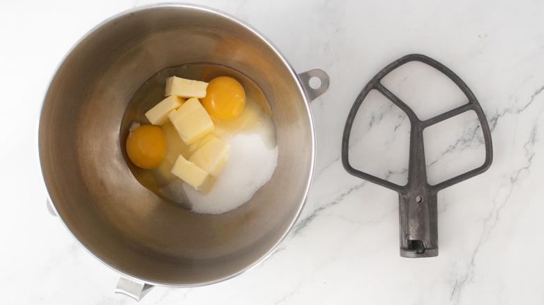 Eggs, butter, and sugar in mixing bowl next to paddle attachment