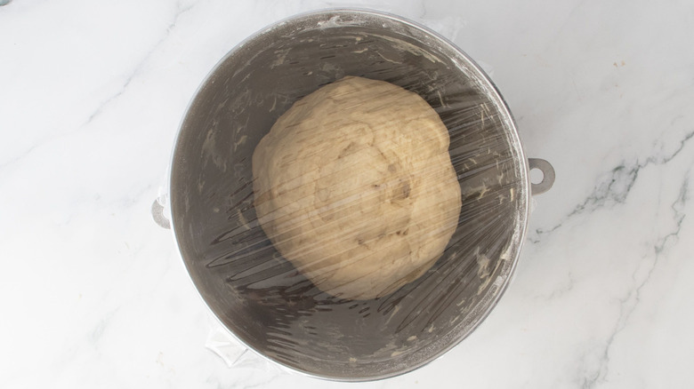 Dough ball in mixing bowl covered with plastic wrap