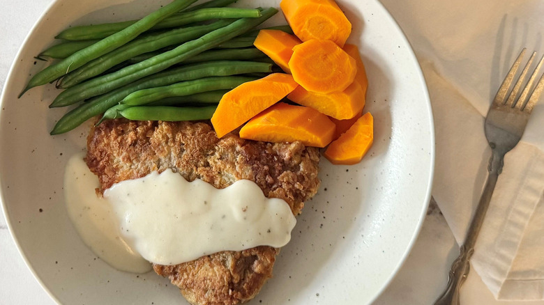 Country fried steak with gravy on plate with green beans and carrots