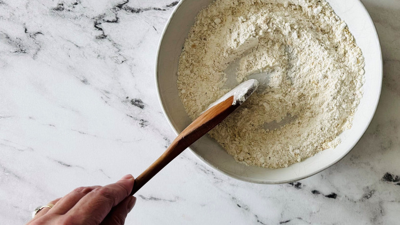 Wooden spoon stirring flour mixture in bowl