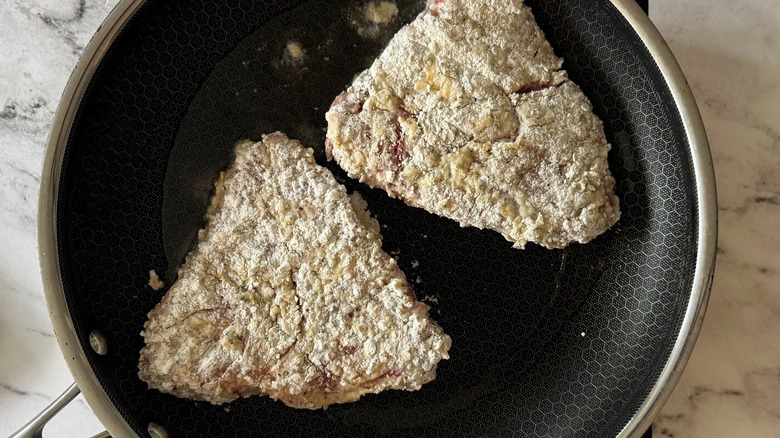 Flour-coated steaks in pan