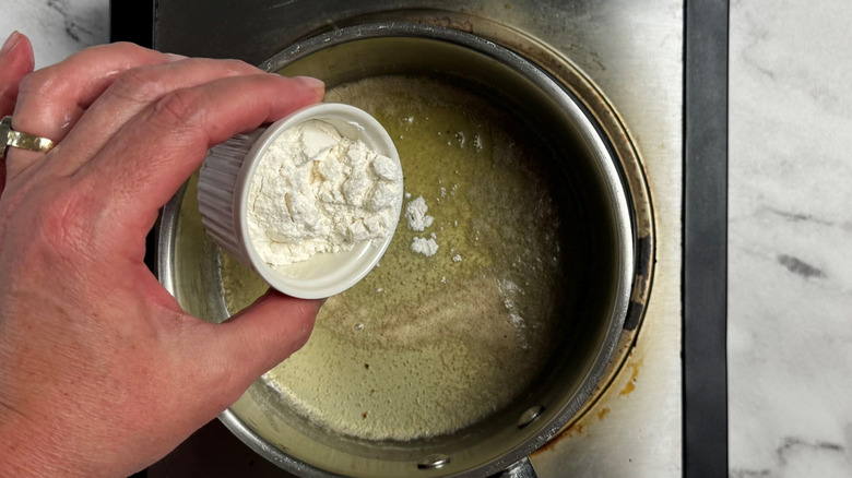 Hand pouring small bowl of flour into saucepan