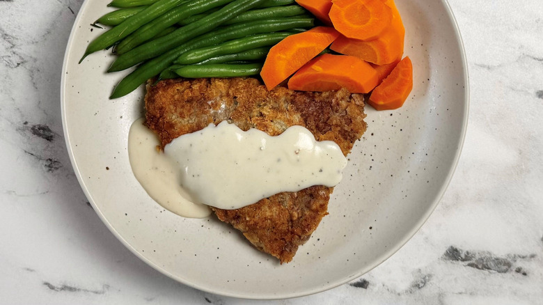 Country fried steak and gravy on plate with green beans and carrots