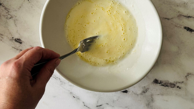 Fork stirring egg mixture in bowl