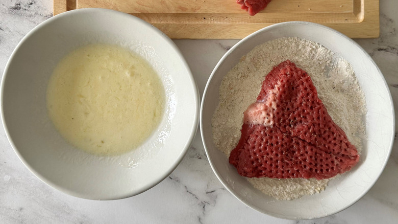 Steak in bowl with flour next to bowl with egg mixture
