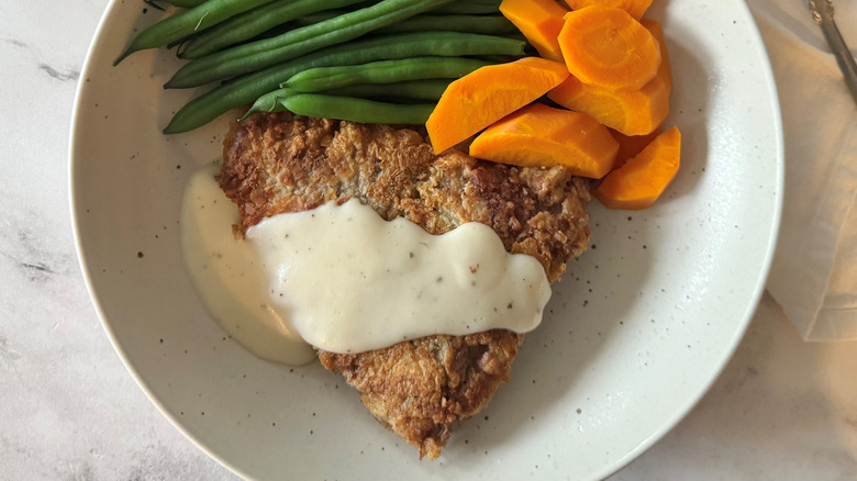 Country fried steak with gravy on plate with green beans and carrots