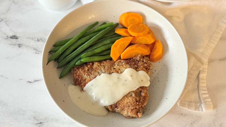 Country fried steak with gravy on plate with green beans and carrots