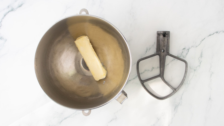 Stick of butter in mixing bowl next to stand mixer paddle attachment