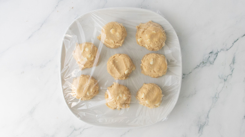 Cookie dough portions on plate covered with plastic wrap