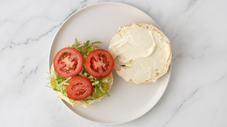 halved burger buns with vegetables and mayo