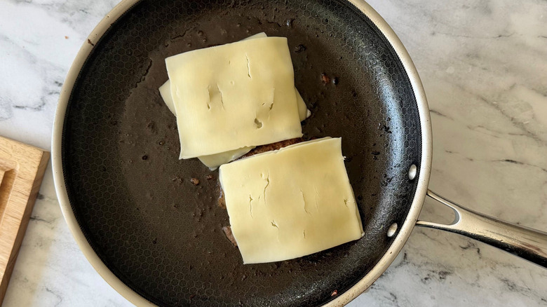 Patties topped with Swiss cheese slices in skillet