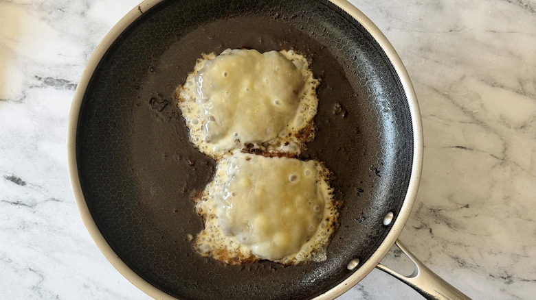 Patties topped with melty cheese in skillet